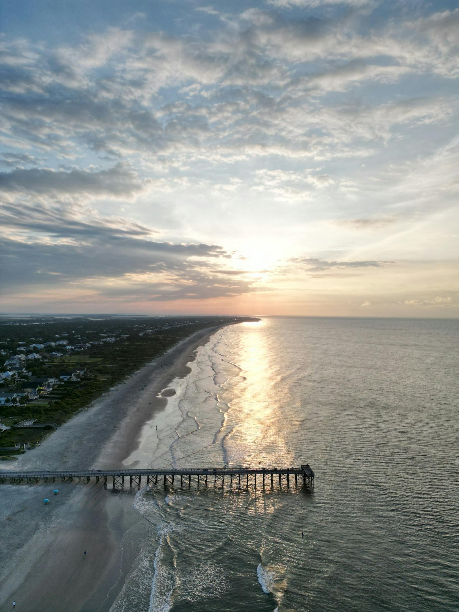 Stunning aerial view of a pier in Charleston, SC, with waves reflecting the sunset glow.